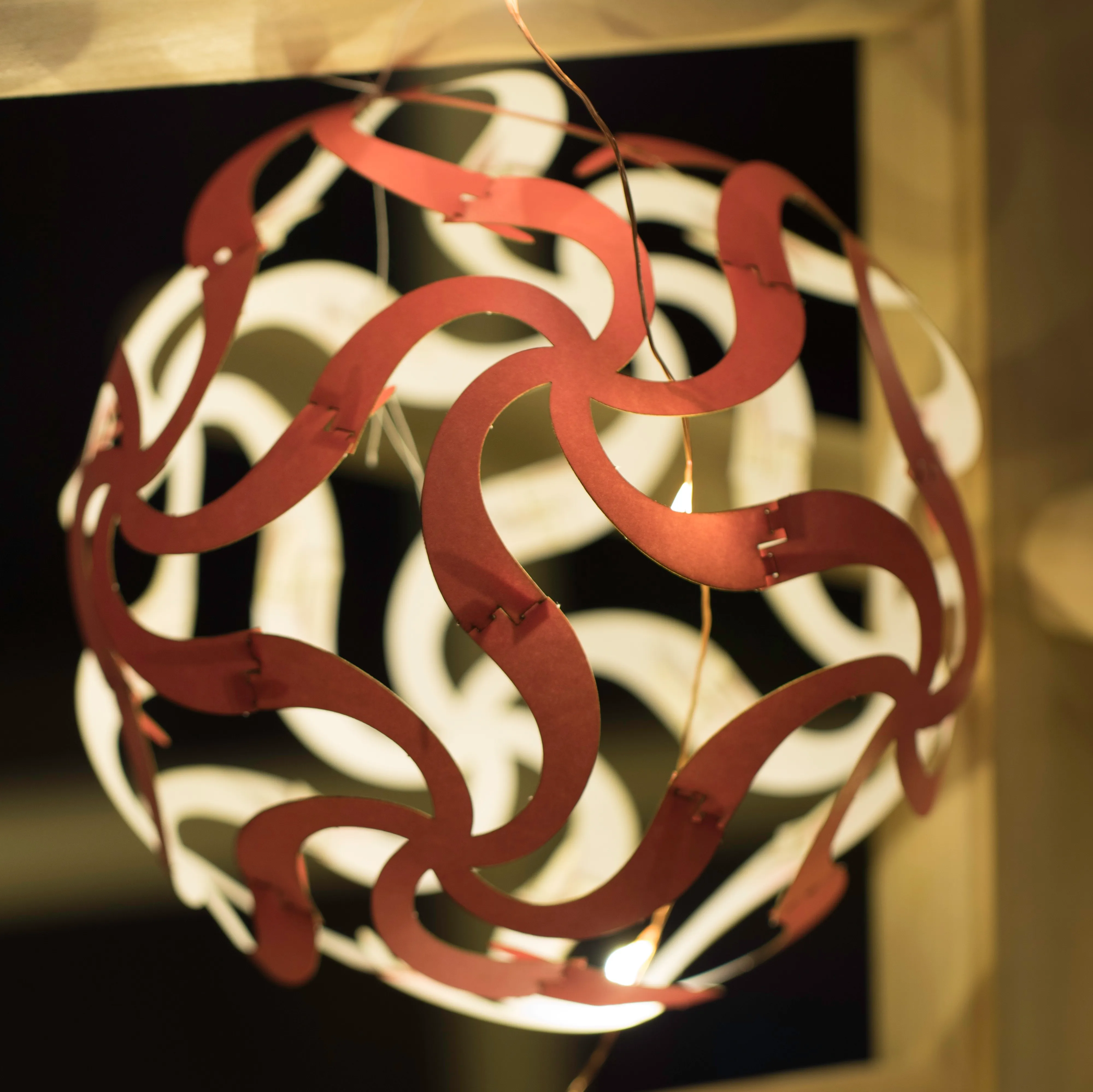 Copper-coloured Curvahedra sphere lit from within, casting patterned shadows on the wall