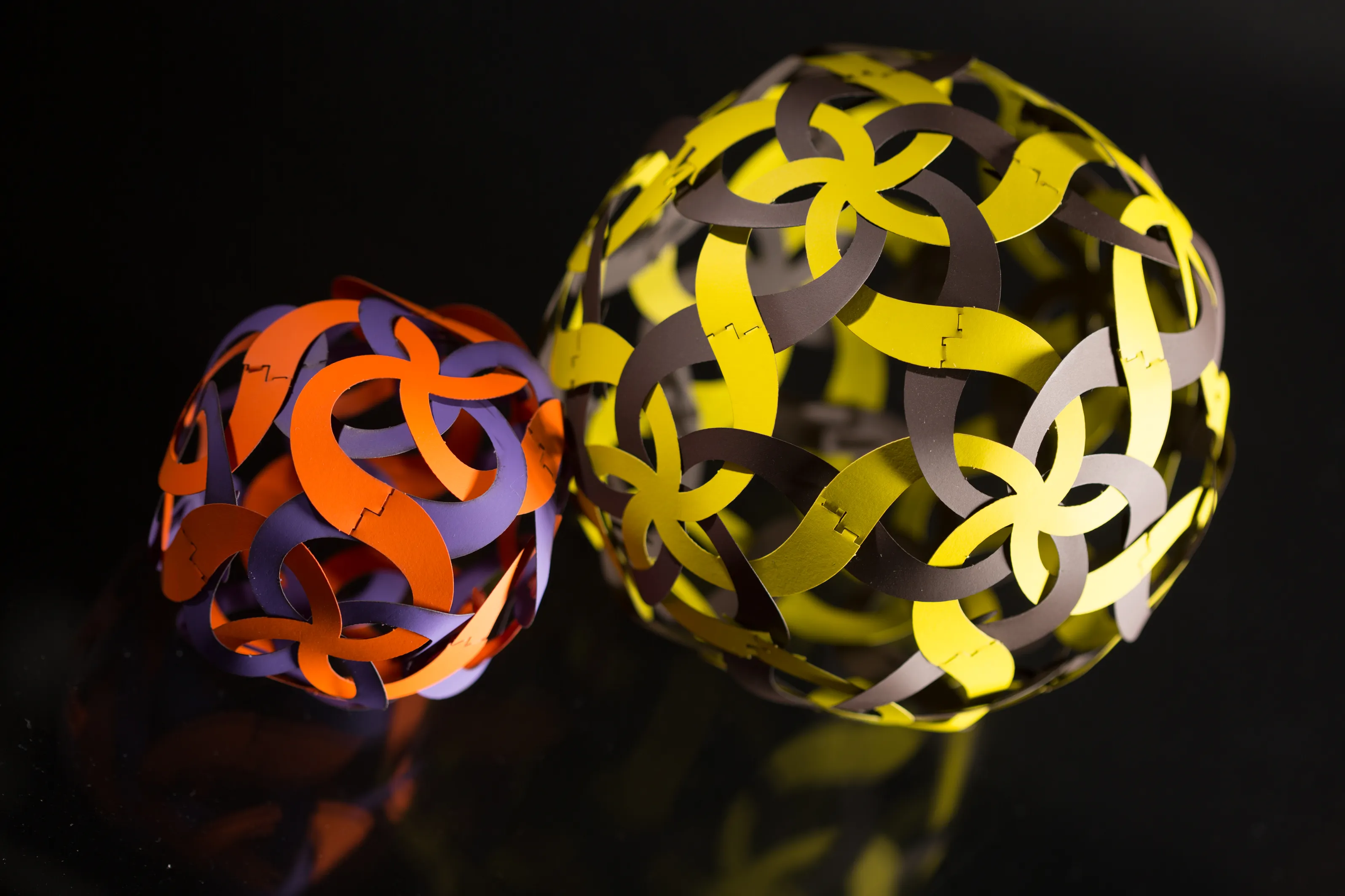 Two Curvahedra spheres,  orange/purple and yellow/dark,  studio portrait against black