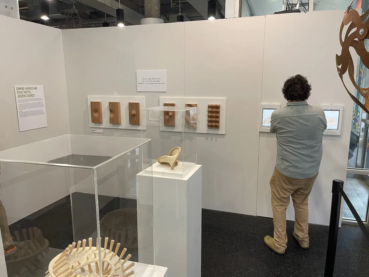 Gallery view with all six Geodesic Boards on the wall, a ceramic on its plinth, and a visitor using the interactive touchscreen