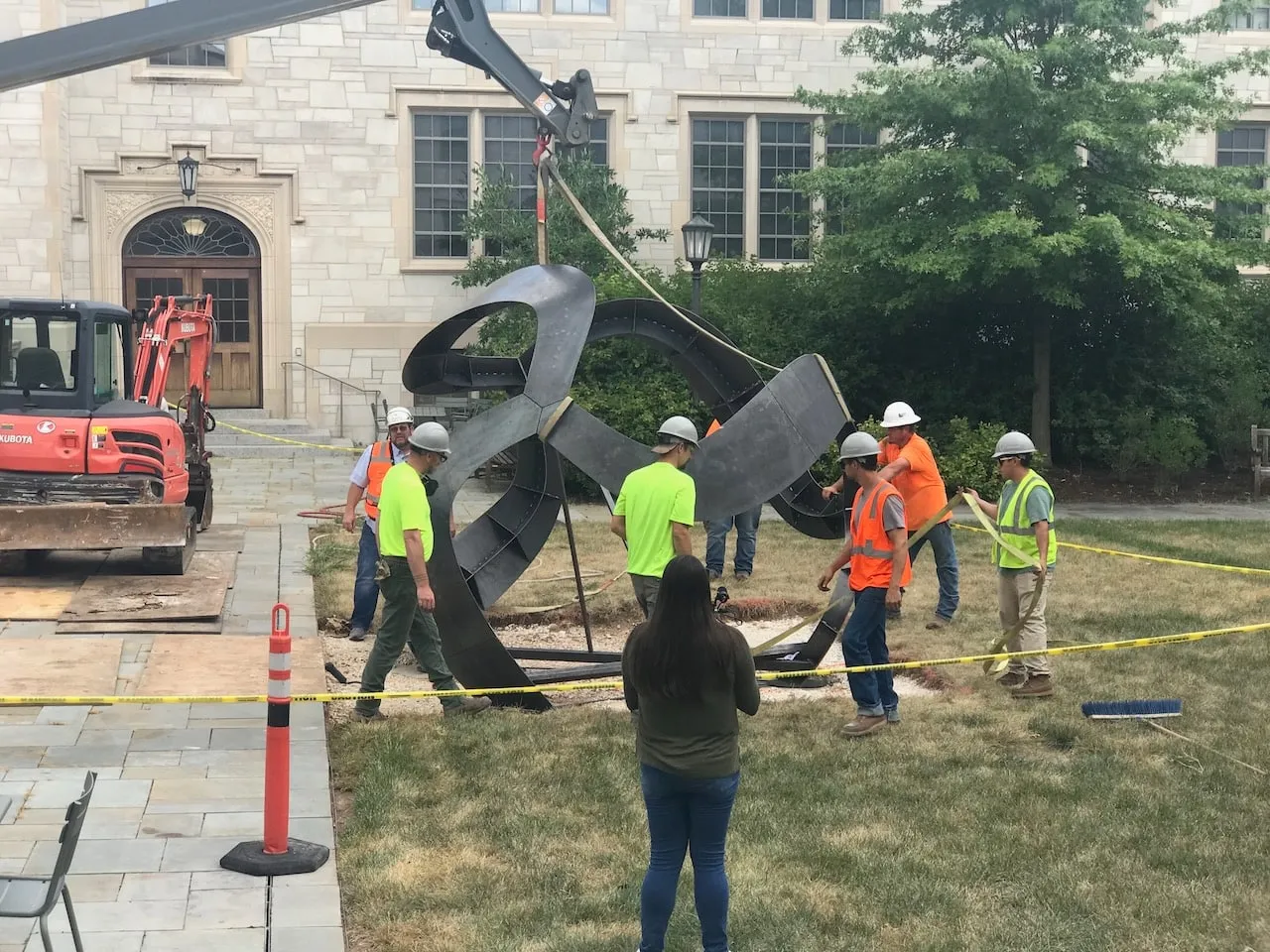 Workers guiding the sculpture into its final position in front of Gearhart Hall,  crane arm visible above, caution tape around the site