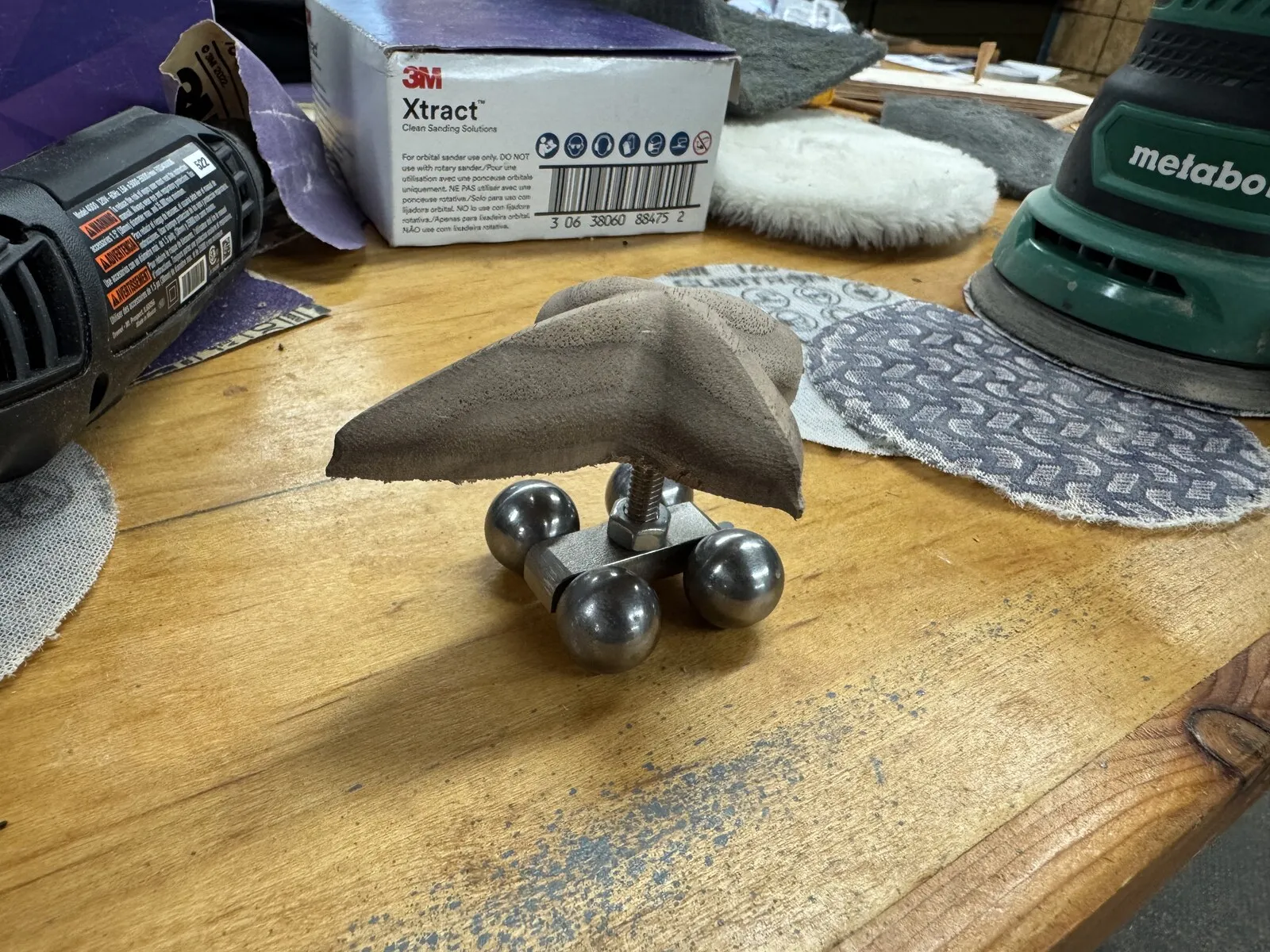 The metal arrow mechanism with four small ball bearings as feet, resting on a workbench