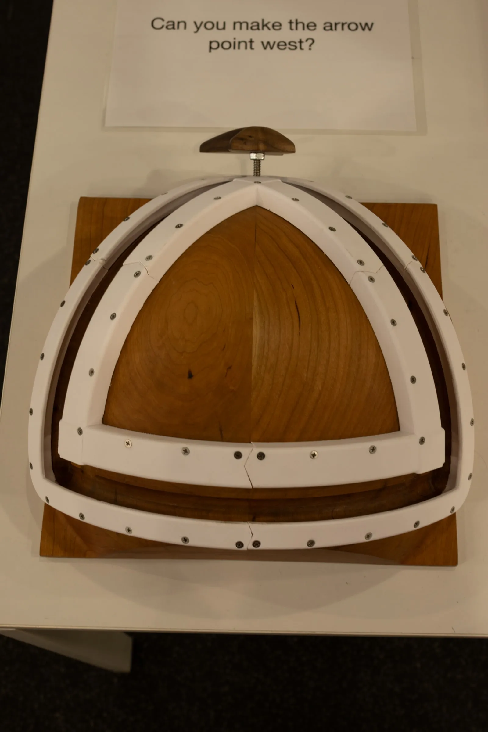 The sphere board from above at MoMath, arrow resting in the tracks, with the prompt "Can you make the arrow point west?"
