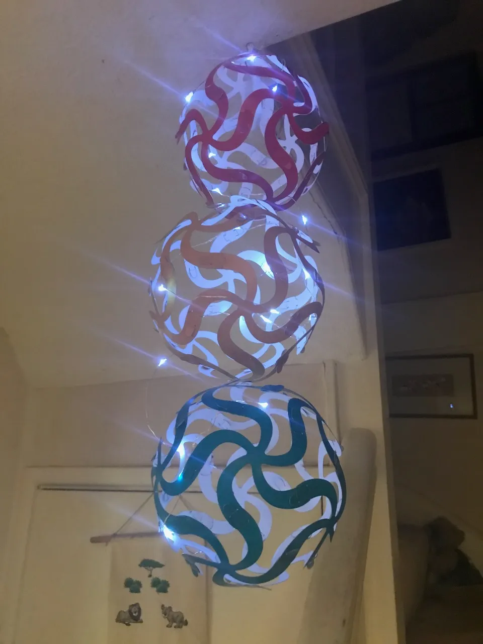 Three Curvahedra spheres,  red, orange, and teal,  hung from a ceiling and lit from within by fairy lights, glowing in a darkened room