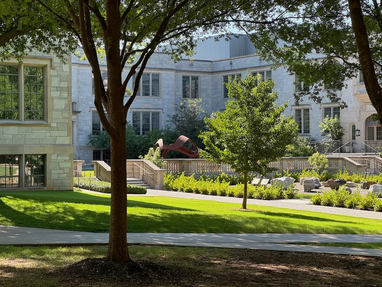 The rust-red Gearhart Hall Curvahedra seen through mature trees from across the University of Arkansas campus