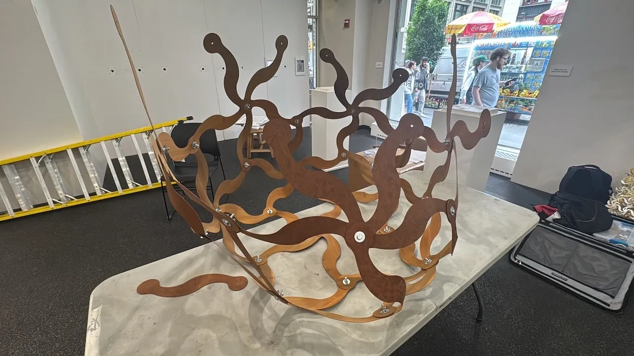 The Curvahedra partially assembled on the gallery table before being hung,  interlocking curved steel and wood elements spread across the surface
