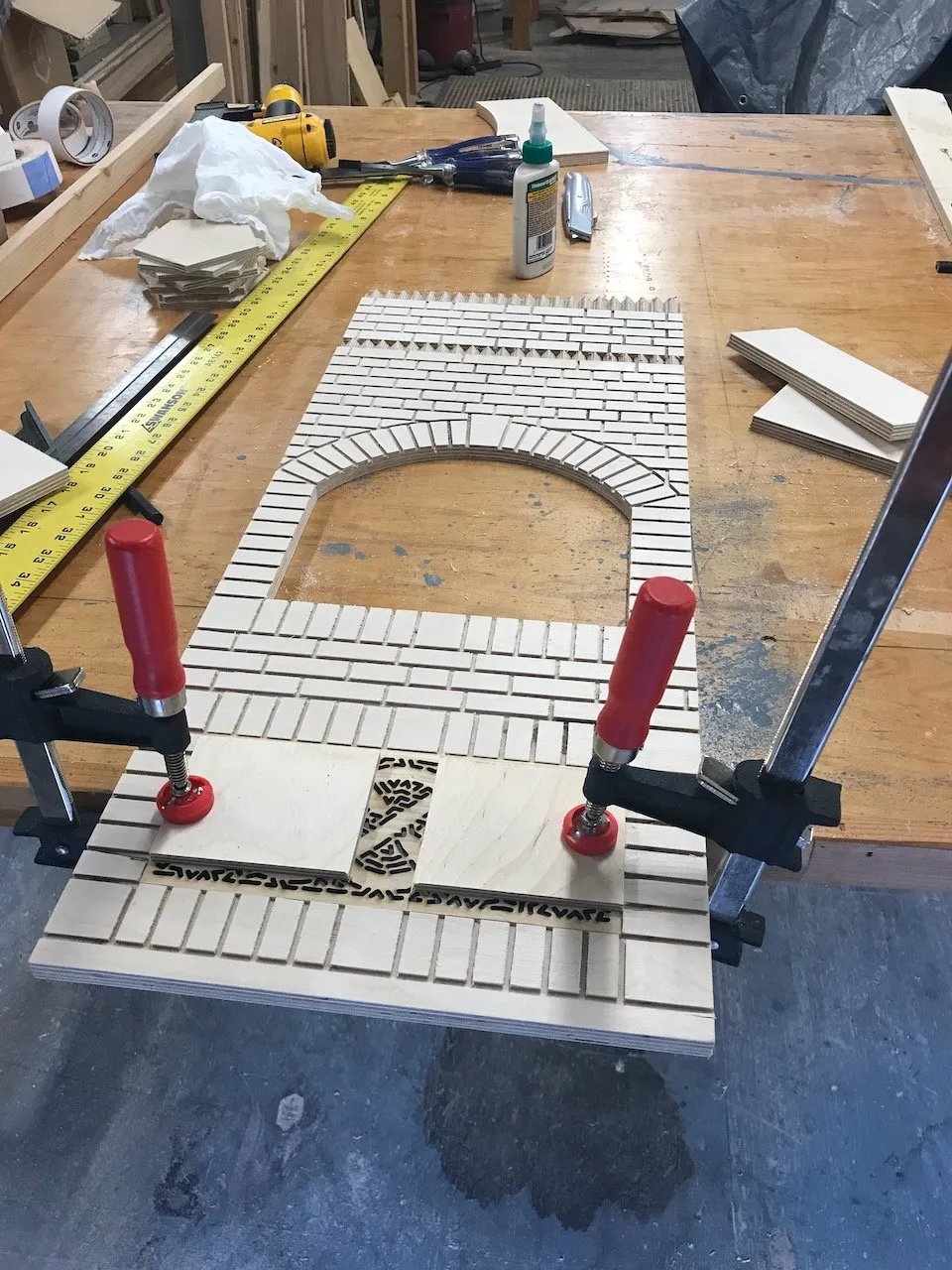 The Bakery's CNC milled brick facade clamped flat on the workshop bench, the arched oven door opening, individual brick tiles, and Celtic knot insert panel at the base