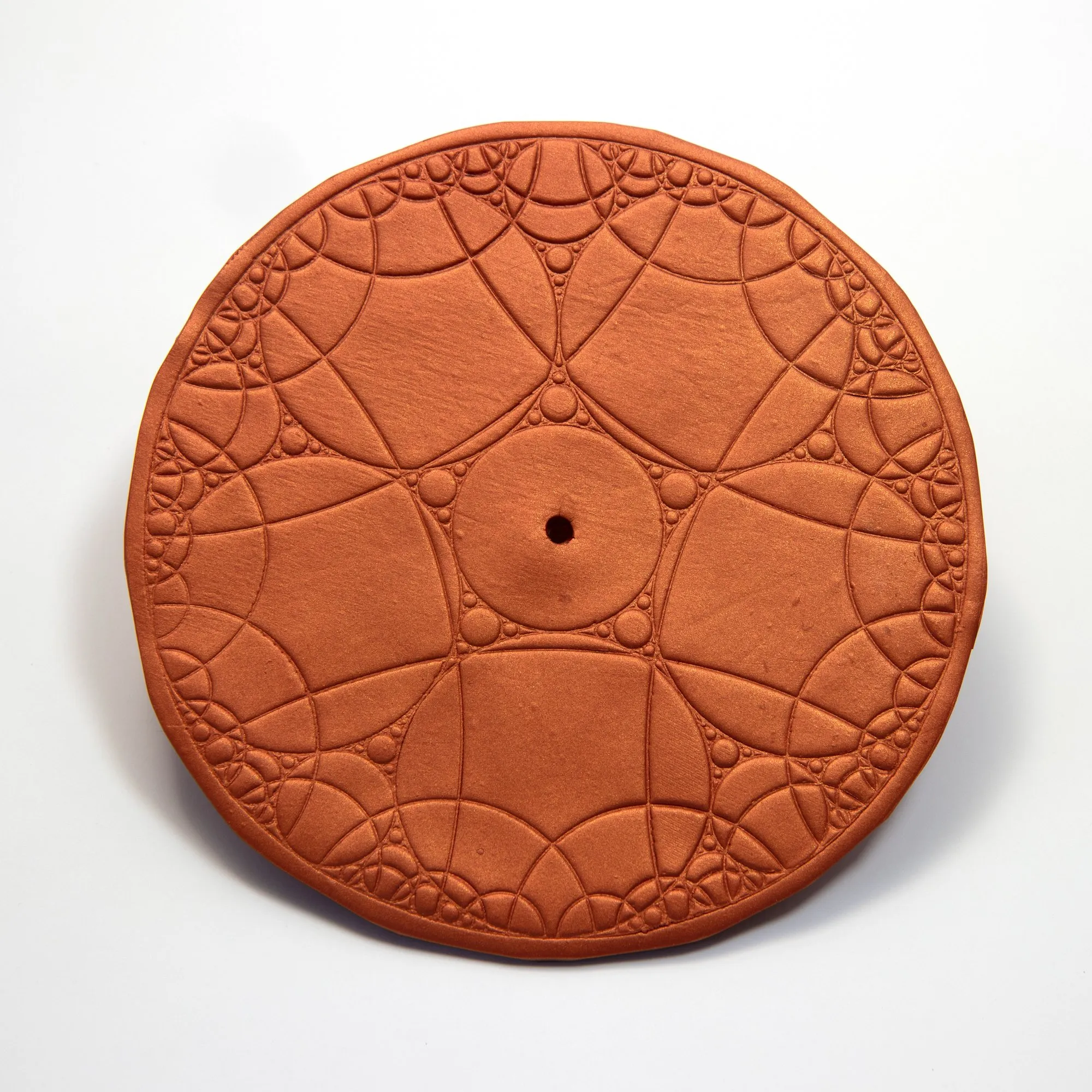 Professional studio shot of the cart wheel; a terracotta-coloured ceramic disk with Apollonian circle-packing pattern, central hole for the axle, on a white background