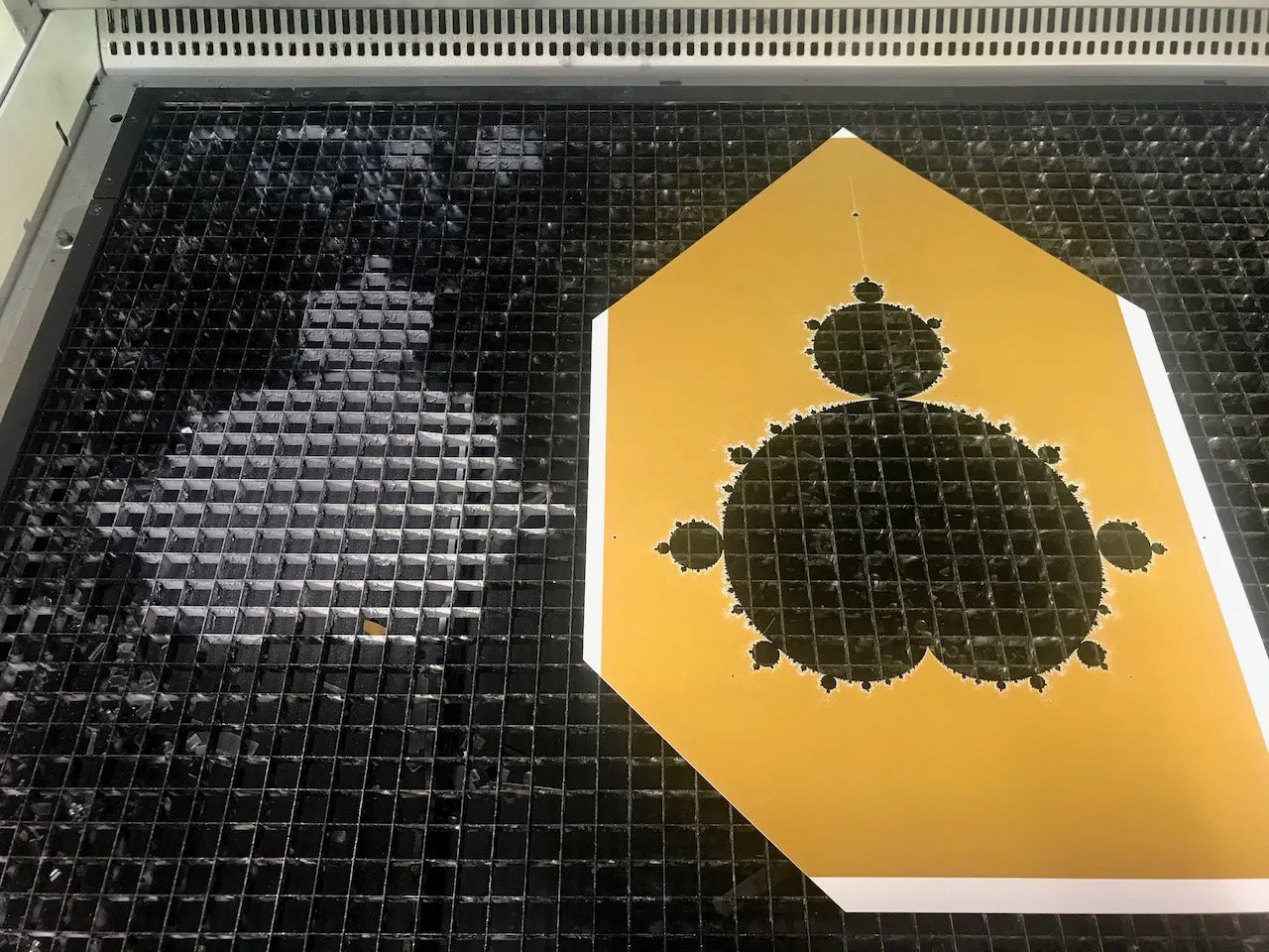 The Bakery roof Mandelbrot hexagonal tile in the laser cutter; the Mandelbrot set rendered in the tile's grid, cut from amber-coloured acrylic