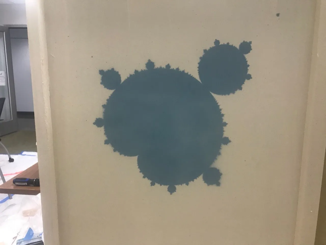 Blue Mandelbrot set graphic painted on a large white foam wall panel at the Duke assembly; the set rendered in brushed blue paint, roughly two feet across