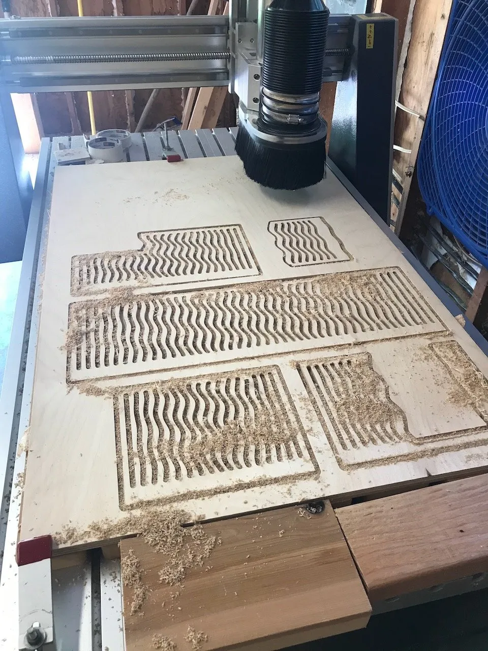 CNC router with all the balcony railing panels for Conway's Curios cut; multiple wave-pattern rectangular panels laid out on the CNC bed with fresh sawdust