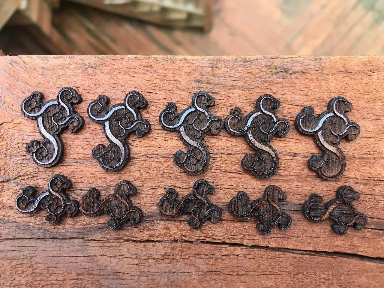 Ten laser-cut S-curve ornaments in two sizes arranged on a cedar board; the Conway's Curios decorative motif, a fractal-like scroll form repeated at different scales