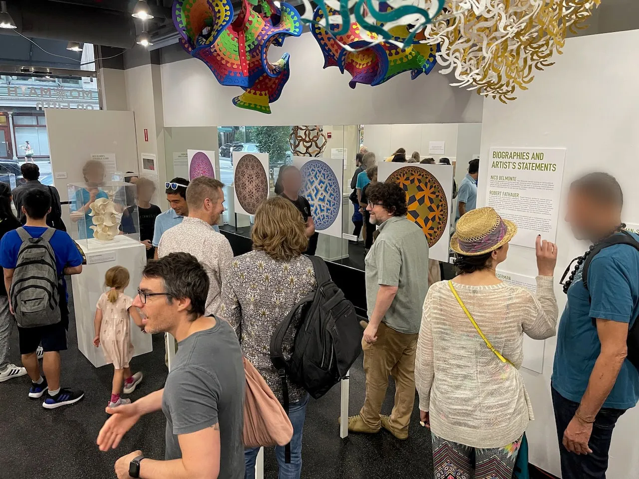 Crowded opening reception: visitors exploring the gallery with Nico Belmonte's hyperbolic floor prints and artist biographies on the wall