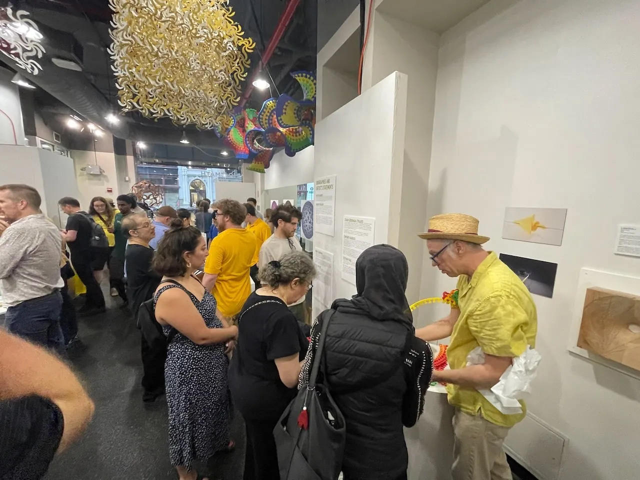 Wide view of a crowded opening reception with the Curvahedra hanging overhead and visitors filling the gallery