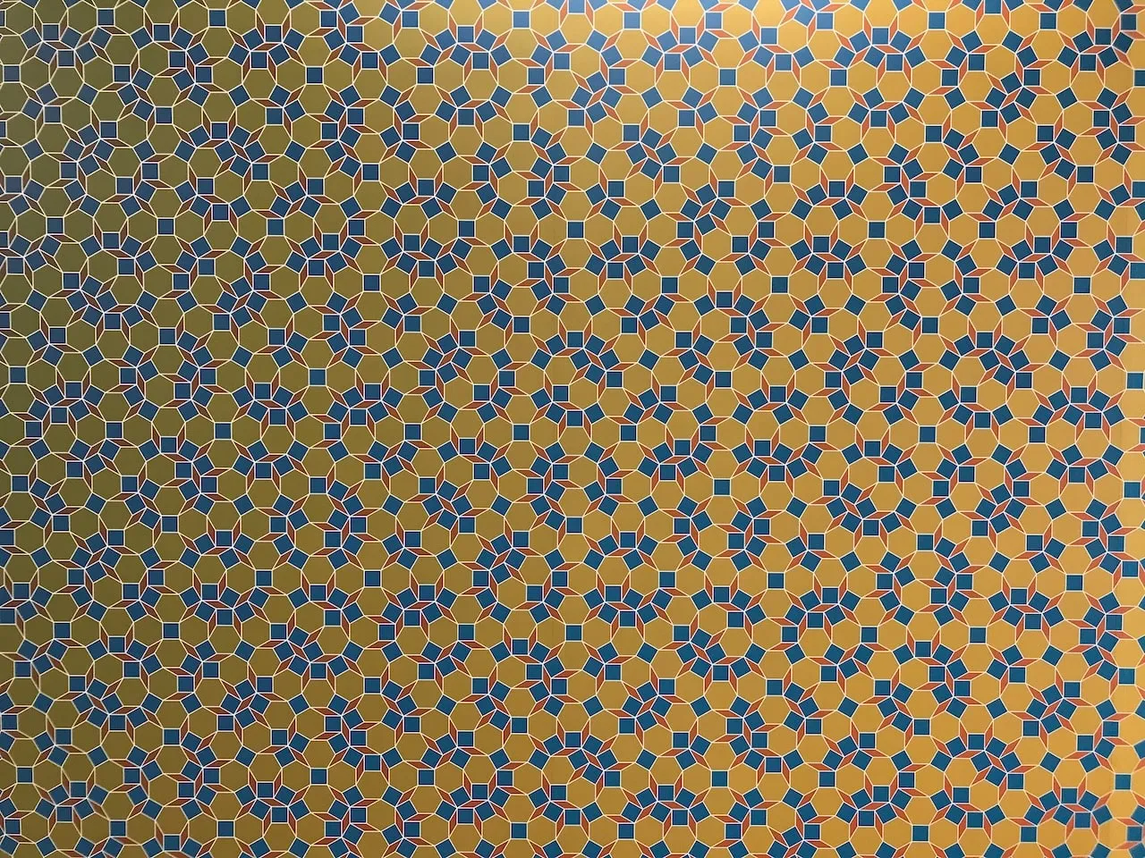 Close detail of the coloured tiling: small blue squares and rounded clusters of tiles scattered across a gold ground, each two-dimensional Socolar tile picked out in colour.