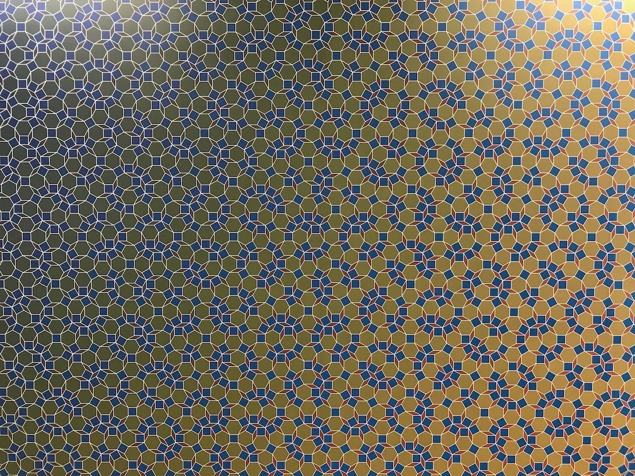 Detail where the tiling gains colour: white-and-blue tile outlines on a dark blue ground at the left give way to solid blue tiles on a gold ground at the right.