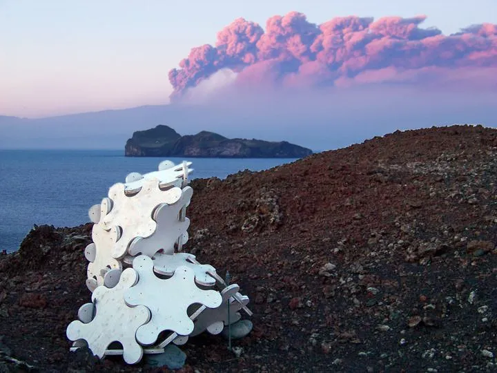 Sculpture System 5 at sunset on Heimaey, the Eyjafjallajökull eruption cloud rising pink across the water behind it