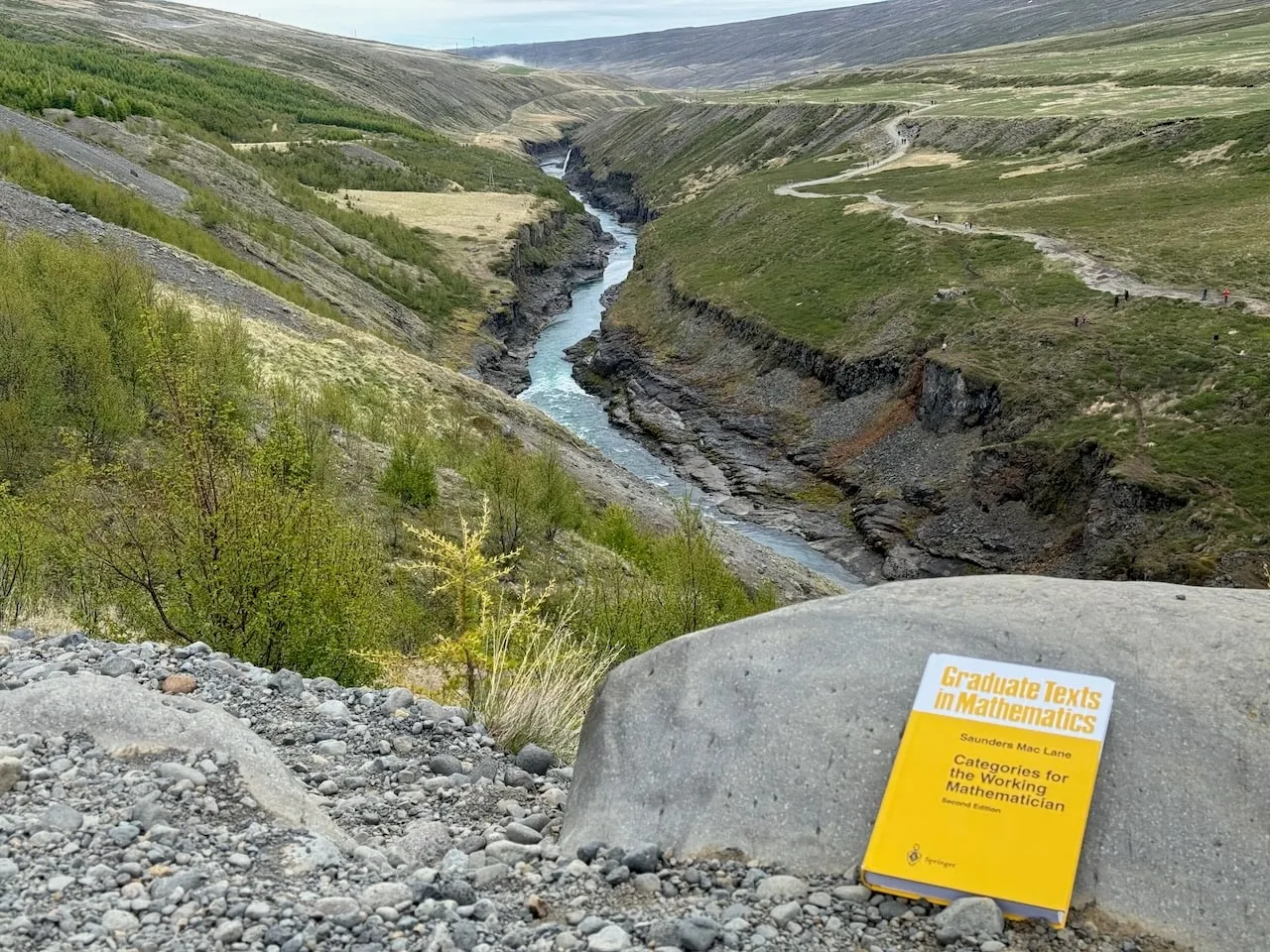 The book on a smooth boulder overlooking a glacial river winding through a steep grassy and basalt canyon