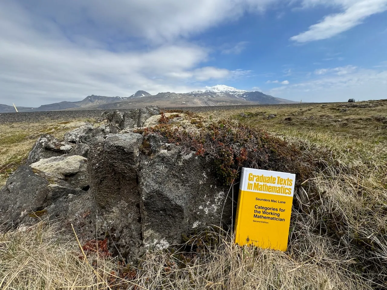 The book leaning against a tussock by a broken lava boulder, brown tundra running back to the snow-streaked Snæfellsjökull massif