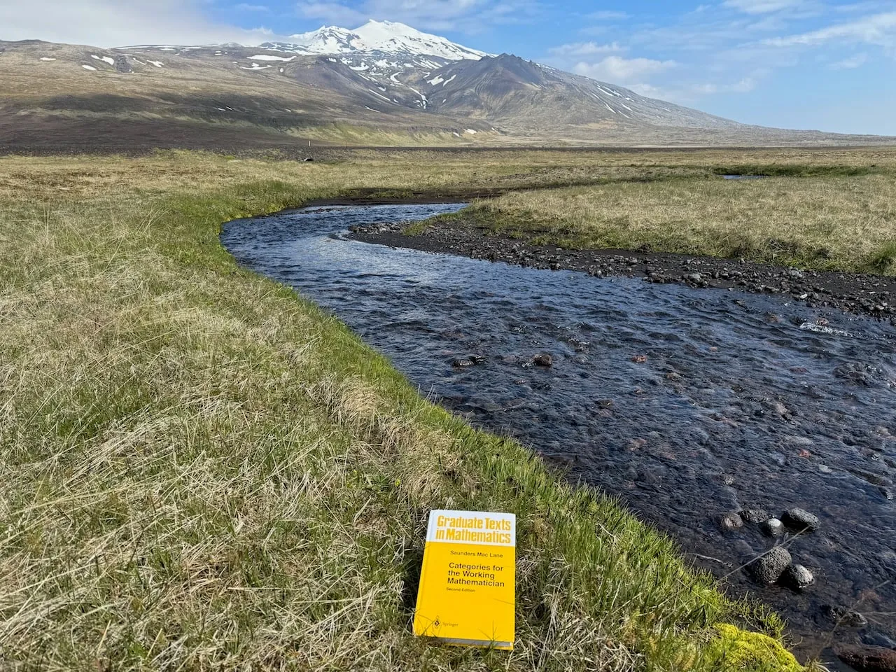 The book in grass beside a dark stream winding through flat tundra toward the snow-capped Snæfellsjökull volcano